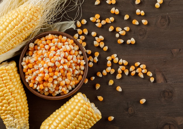 Corn grains in a clay plate with cobs flat lay on a wooden table