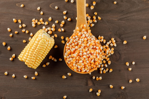 Corn grains with cob slice in a wooden spoon on wooden table, flat lay.