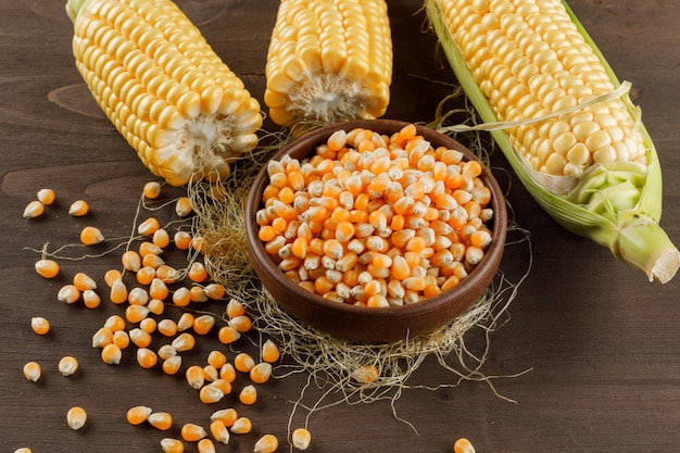 Corn grains with cobs in a clay plate on wooden table, high angle view.