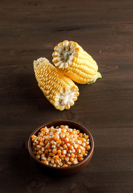 Corn grains with slices in a clay plate on wooden table, high angle view.