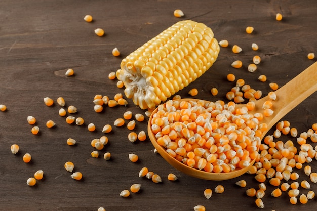 Corn grains in a wooden spoon with cob slice high angle view on a wooden table