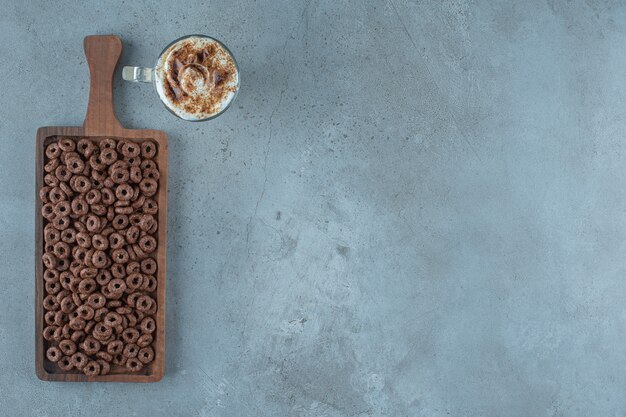 Corn ring in a board next to glass of milk coffee , on the blue background.