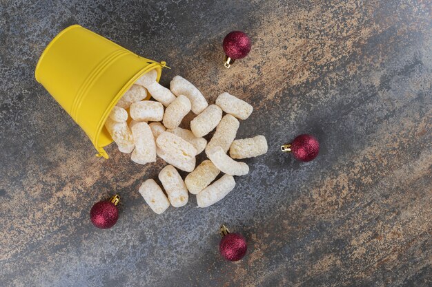 Corn snacks pouring out of a bucket next to christmas baubles on marble surface