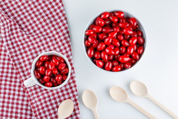 Cornel berries in  bowl and cup with wooden spoons on picnic cloth and white