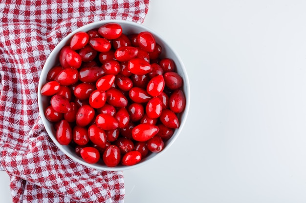 Cornel berries in a bowl on picnic cloth and white. flat lay.