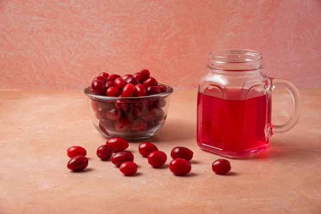 Free photo cornel berries in the cup and juice in the glass jar.