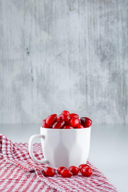 Free photo cornel berries in a cup with picnic cloth side view on grey and white