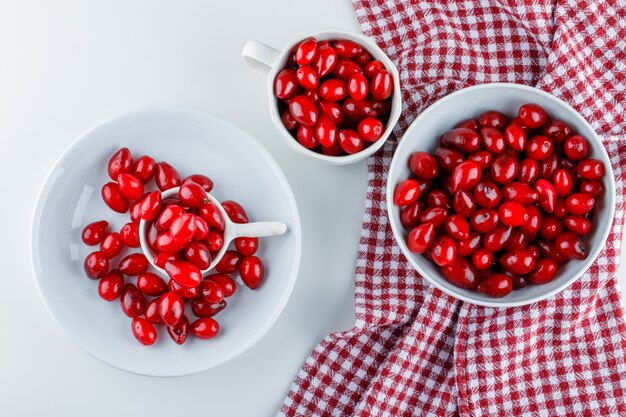 Cornel berries in different plates on white and picnic cloth. flat lay.