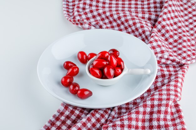 Cornel berries in scoop and plate on white and picnic cloth. high angle view.