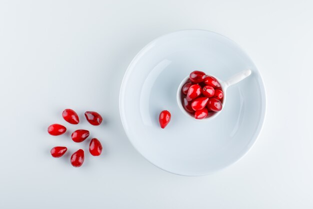 Cornel berries in a scoop with plate top view on white