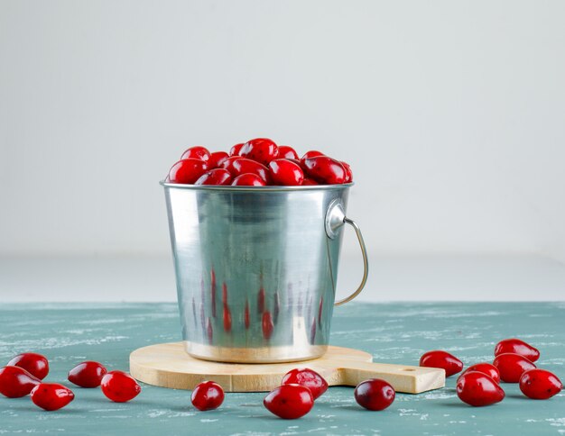 Cornel berries with cutting board in a bucket on plaster and white, side view.