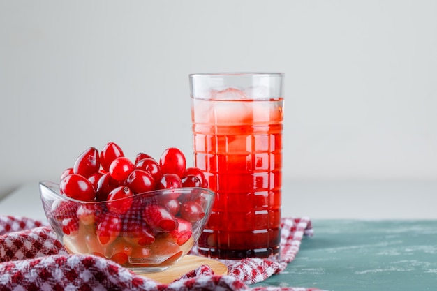 Cornel berries with drink, cutting board, picnic cloth in a bowl on plaster and white, side view.