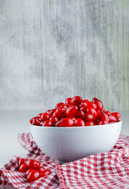 Cornel berries with picnic cloth in bowl on white and grey, side view.