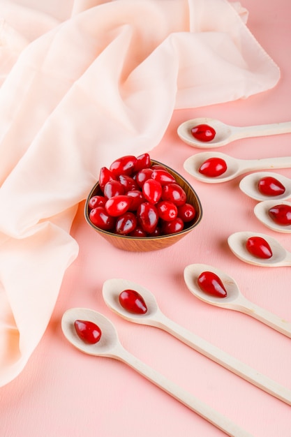 Cornel berries in wooden spoons and bowl on pink and textile. high angle view.