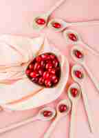 Free photo cornel berries in wooden spoons and bowl on pink and textile, top view.