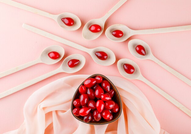 Cornel berries in wooden spoons and bowl on pink and textile.