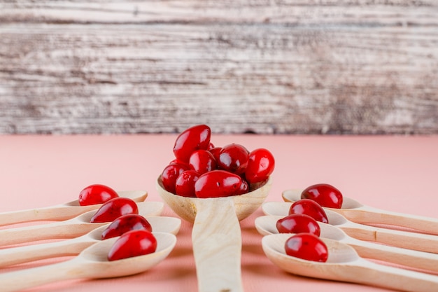 Cornel berries in wooden spoons on pink and wood. high angle view.