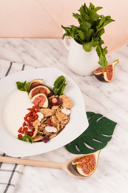 Cornflakes with fig fruit and mint leaves on decorated plate over marble worktop