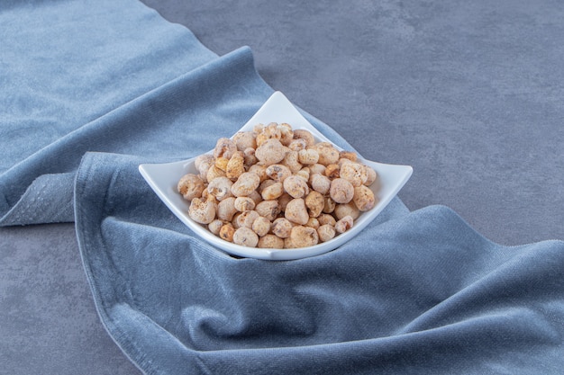 Cornflakes with muesli in a bowl on a piece of fabric , on the marble background.