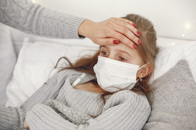 Coronavirus in a child. Mother with daughter. Child lying in a bed. Woman in a medical mask.