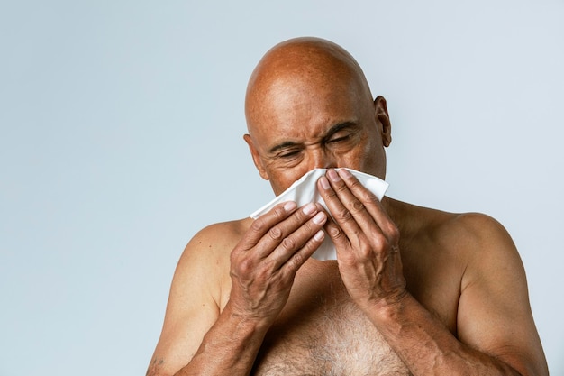 Coronavirus infected senior man blowing nose into a tissue paper