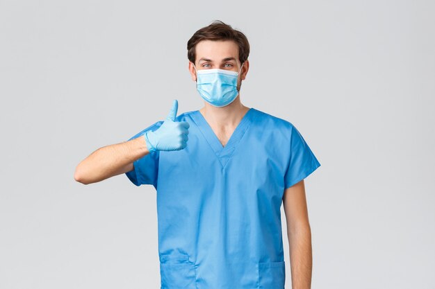 코로나바이러스 발병, 질병과 싸우는 의료 종사자, 병원 개념. covid-19 동안 간호사와 의료 종사자를 지원하도록 요청하는 파란색 수술복을 입은 친절한 의사가 엄지손가락을 위로 보여줍니다.