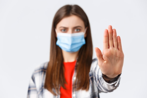 コロナウイルスの発生、検疫の余暇、社会的距離と感情の概念。深刻な女性のクローズアップは、手のひらを伸ばして、悪い決定をやめたり、制限したり、禁止したり、医療用マスクを着用したりします。