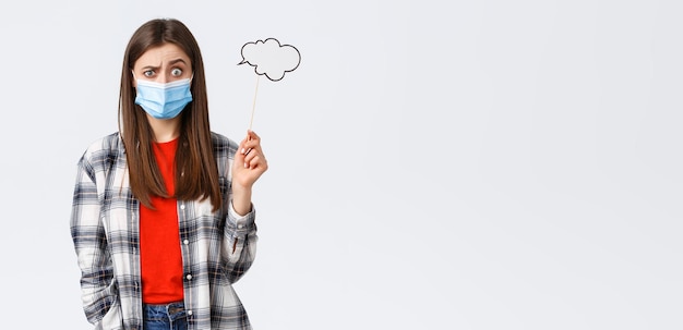 Coronavirus outbreak leisure on quarantine social distancing and emotions concept Confused and clueless young girl in medical mask have no ideas hold cloud stick near head