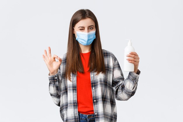 Coronavirus outbreak, leisure on quarantine, social distancing and emotions concept. Cute caucasian woman in medical mask assure this soap is good for preventing virus, show oka sign
