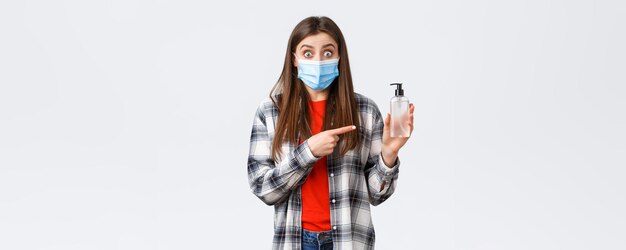 Coronavirus outbreak leisure on quarantine social distancing and emotions concept Excited and astonished young woman in medical mask pointing at hand sanitizer recommend product