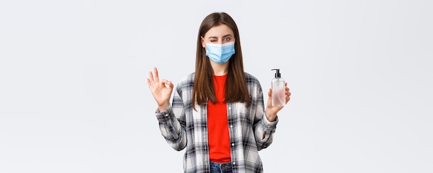 検疫の社会的距離と感情の概念に関するコロナウイルスの発生の余暇問題ありません医療マスクの満足しているかわいい女の子は、手の消毒剤を宣伝するように大丈夫なサインとウィンクを示します