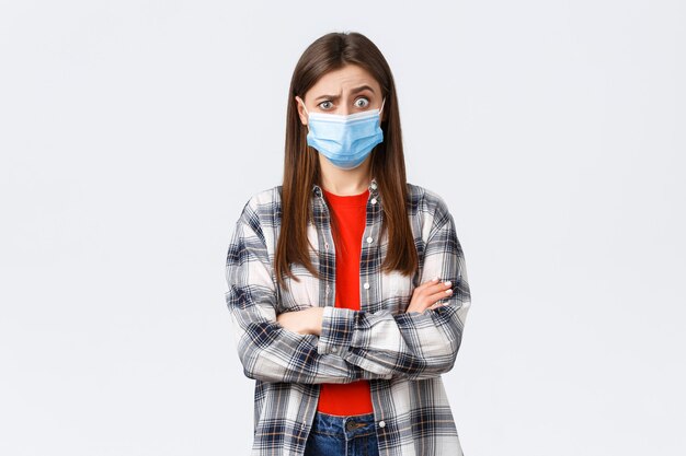 Coronavirus outbreak, leisure on quarantine, social distancing and emotions concept. Shocked and confused young pretty teenage girl hear strange news, raise eyebrows puzzled, wear medical mask
