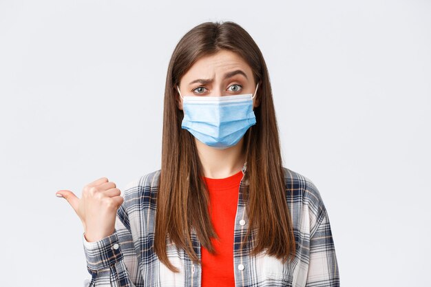 Coronavirus outbreak, leisure on quarantine, social distancing and emotions concept. Skeptical young woman in medical mask express disbelief towards banner to the left, pointing doubtful