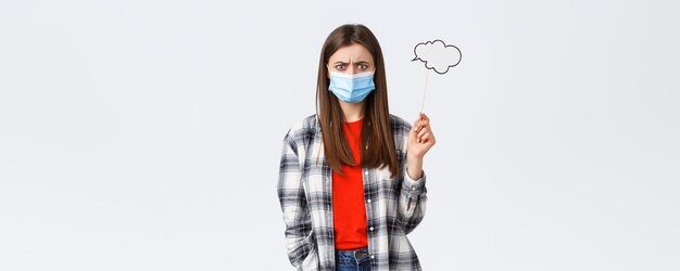 Coronavirus outbreak leisure on quarantine social distancing and emotions concept Troubled young woman in medical mask frowing upset or disappointed hold comment cloud stick near head