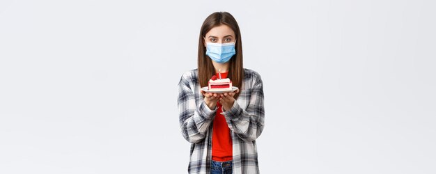 社会的な距離と休日のお祝いのコンセプトのコロナウイルス発生ライフスタイル検疫中に一人で誕生日を祝う医療マスクのかわいい若い女性はbdayケーキを保持します