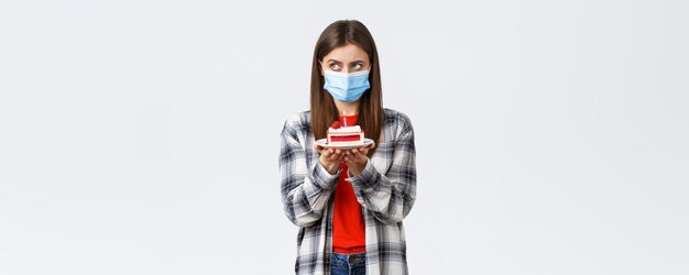 社会的距離と休日のお祝いのコンセプトのコロナウイルス発生ライフスタイル医療マスクの深刻な誕生日の女の子は、火のついたキャンドルでbdayケーキを保持するように願い事を考えることに焦点を当てています