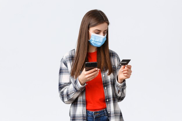 Coronavirus outbreak, working from home, online shopping and contactless payment concept. Girl in medical mask pay order groceries from grocery store to deliver, hold mobile phone and credit card.