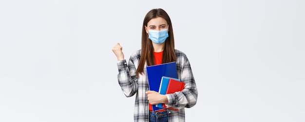 Free photo coronavirus pandemic covid19 education and back to school concept rejoicing cheerful female student in medical mask happy entering cool university fist pump in success holding notebooks