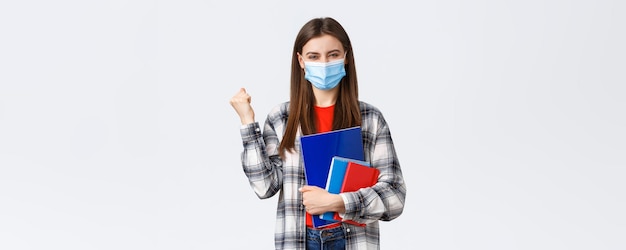 Coronavirus pandemic covid19 education and back to school concept Rejoicing cheerful female student in medical mask happy entering cool university fist pump in success holding notebooks