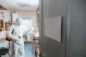 Free photo coronavirus pandemic. disinfector in a protective suit and mask sprays disinfectants in the house or office