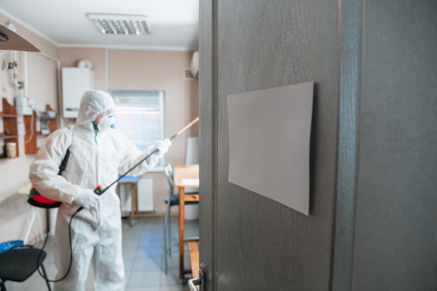 Coronavirus Pandemic. disinfector in a protective suit and mask sprays disinfectants in the house or office