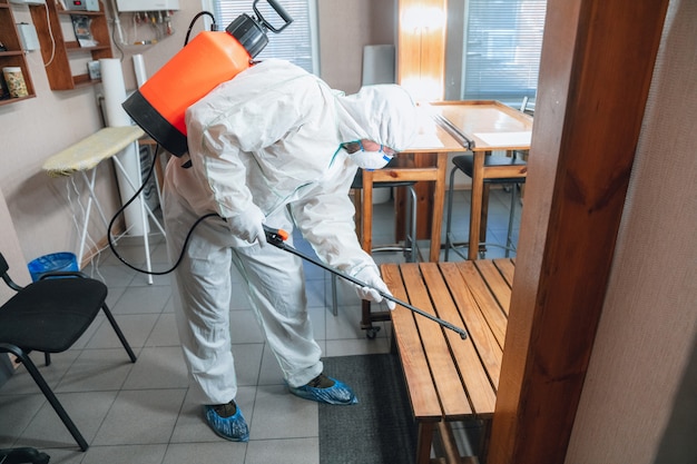 コロナウイルスパンデミック。保護スーツを着た消毒器とマスクが家またはオフィスに消毒剤をスプレーする