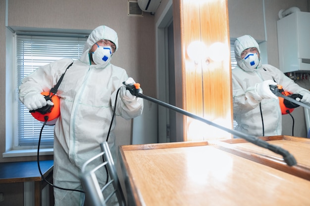 コロナウイルスパンデミック。保護スーツを着た消毒器とマスクが家またはオフィスに消毒剤をスプレーする