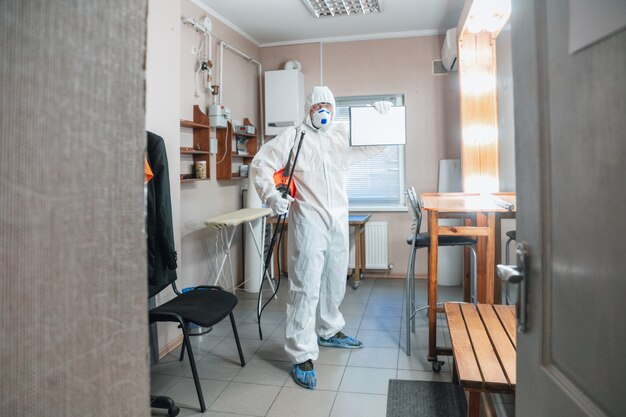 Coronavirus Pandemic. disinfector in a protective suit and mask sprays disinfectants in the house or office