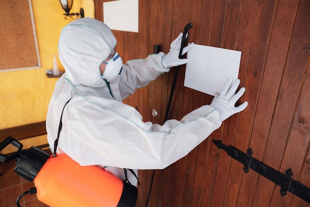 Free photo coronavirus pandemic. disinfector in a protective suit and mask sprays disinfectants in the house or office