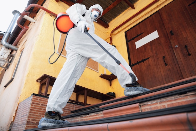 Coronavirus Pandemic. disinfector in a protective suit and mask sprays disinfectants in the house or office