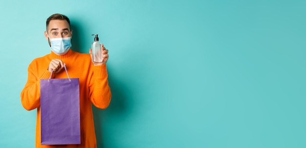 Free photo coronavirus pandemic and lifestyle concept man in face mask showing shopping bag and hand sanitizer