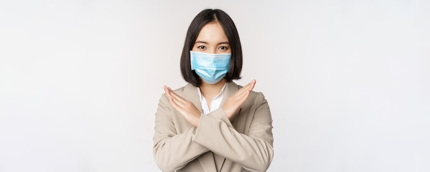Coronavirus e concetto di posto di lavoro l'immagine di una donna d'affari asiatica in maschera medica mostra la croce di arresto che proibisce il gesto si erge su sfondo bianco