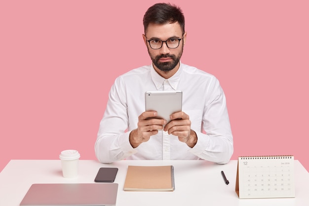 Corporate manager uses touchpad for accounting, wears optical glasses and white shirt, checks report, analyzes budget