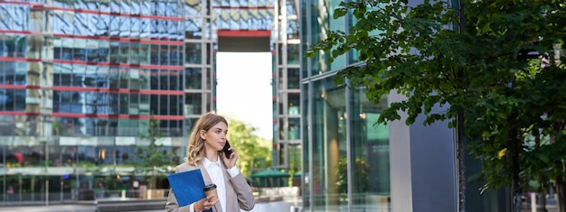 Foto gratuita donna aziendale in giacca e cravatta che cammina nel centro della città con documenti di lavoro e chiamate al cellulare